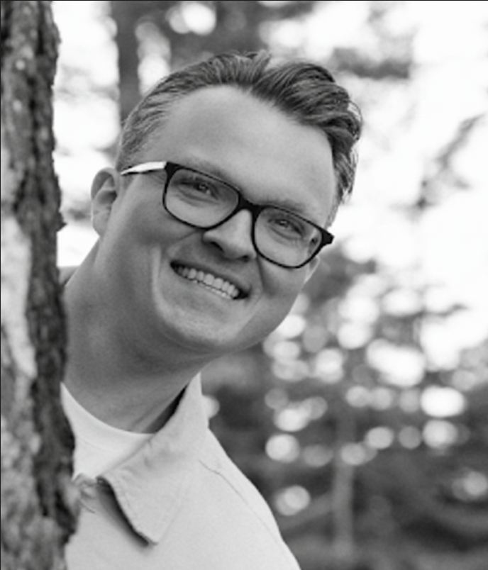 Adrian Budny smiling while peeking from behind a tree.
